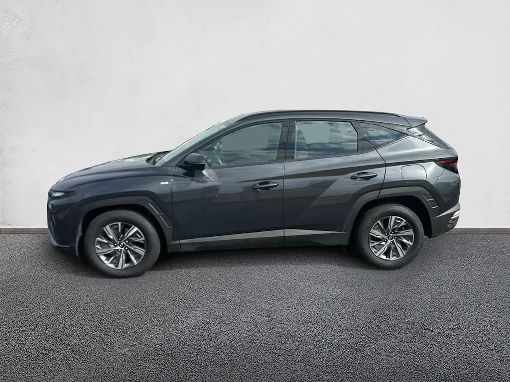 Vue de profil côté gauche d'un Hyundai Tucson gris 2023, version hybride diesel avec jantes alliage et lignes anguleuses marquées.