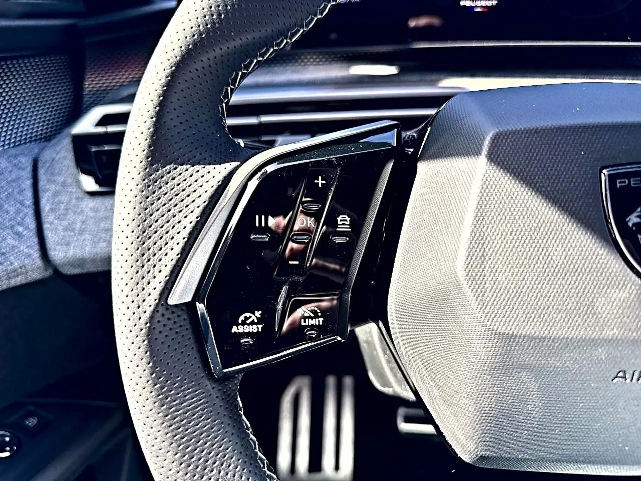Gros plan sur le volant cuir perforé noir du Peugeot 5008 Hybrid, avec commandes multifonctions visibles à gauche.