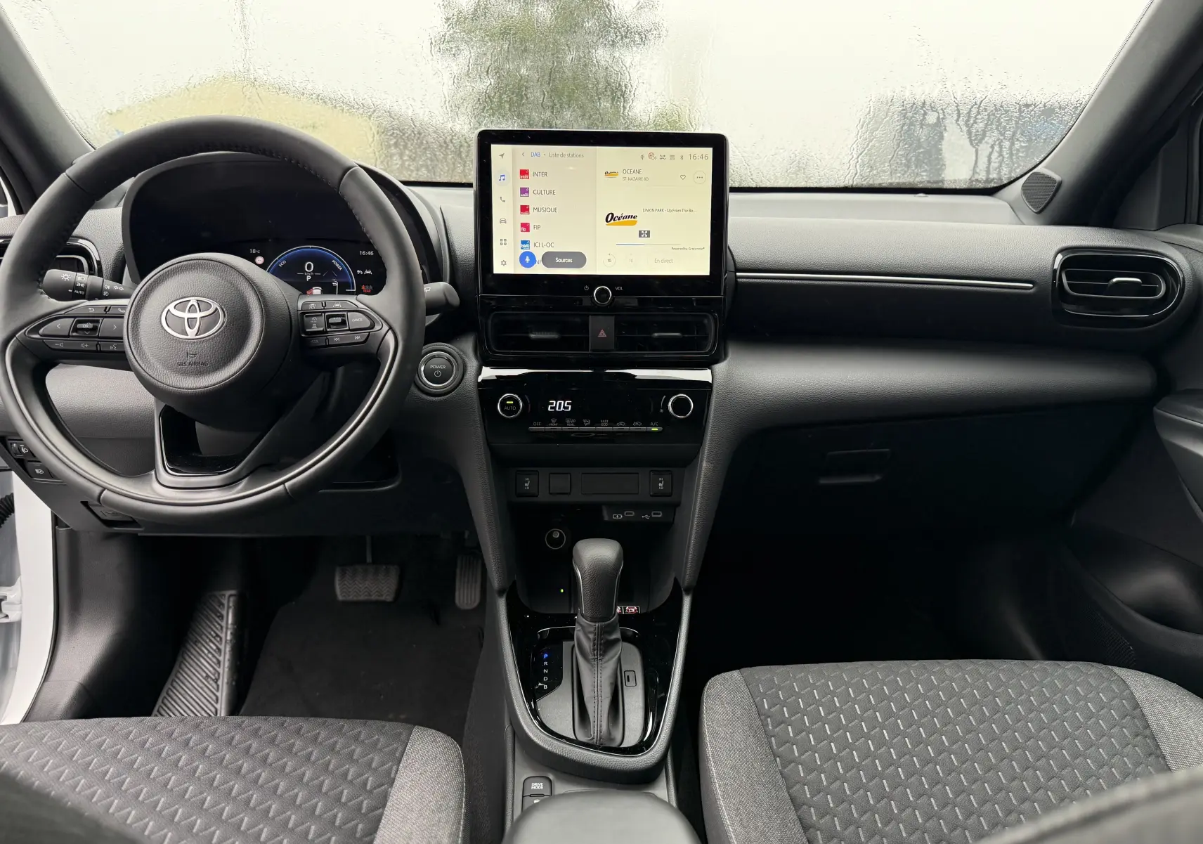 Vue frontale de l'habitacle de la Toyota Yaris Cross blanche, montrant le volant, l'écran tactile et la console centrale moderne.