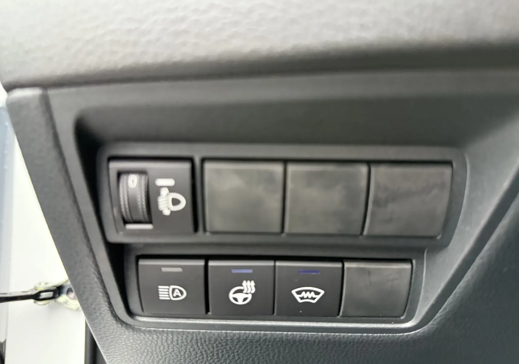 Panneau de commandes noires avec boutons de réglage des phares, volant chauffant et dégivrage sur Toyota Yaris Cross blanc côté gauche.