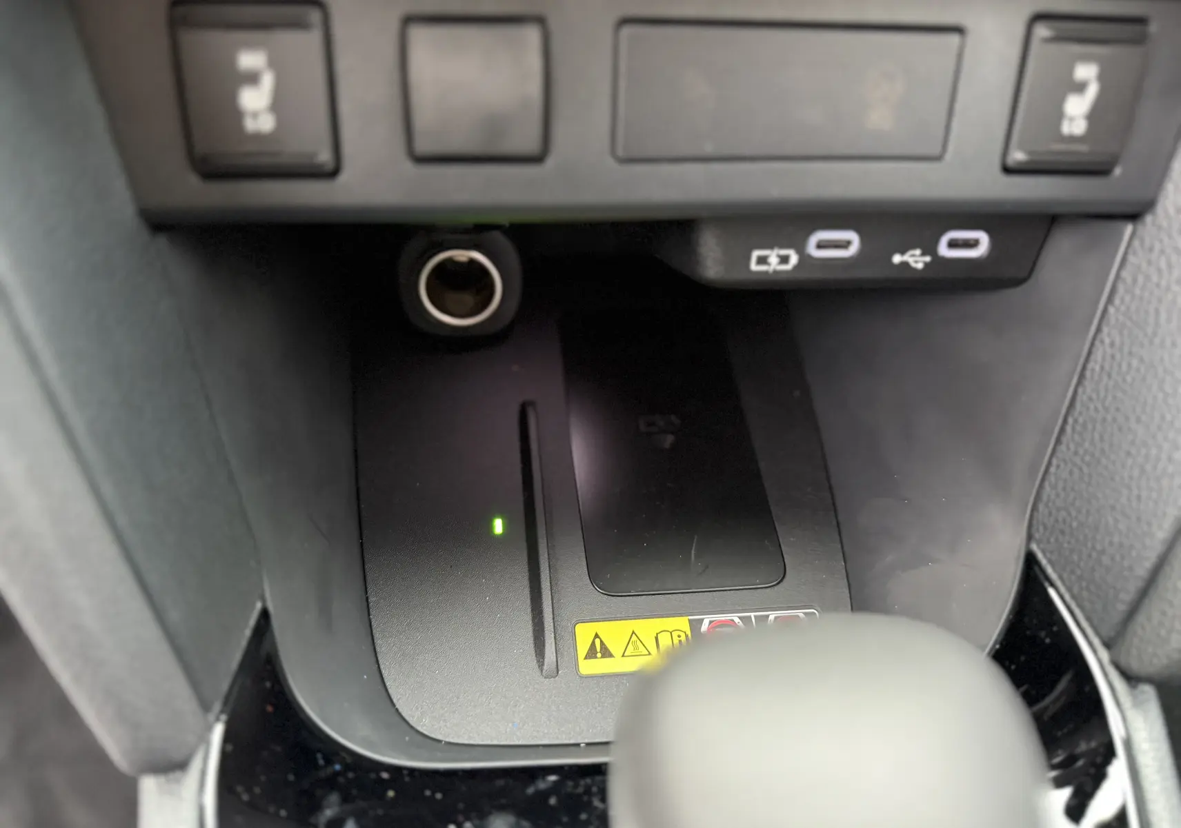 Gros plan sur la console centrale noire de la Toyota Yaris Cross 130 CH Design MY25, montrant prises USB et chargeur sans fil.