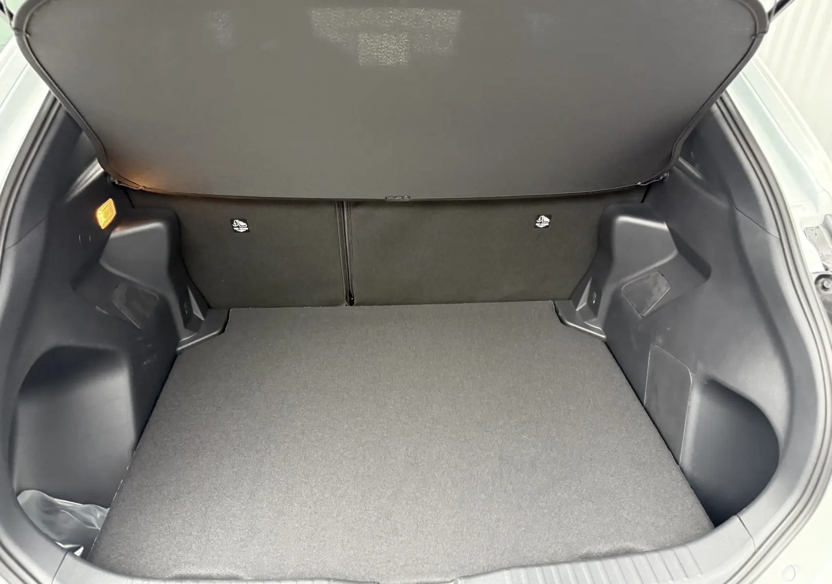 Coffre ouvert de la Toyota Yaris Cross 130 CH Design blanc pur, montrant un espace de chargement propre et bien agencé.