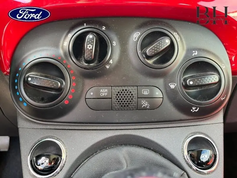 Gros plan sur les commandes de climatisation noires du tableau de bord d'une FIAT 500 noire, avec réglages manuels visibles.