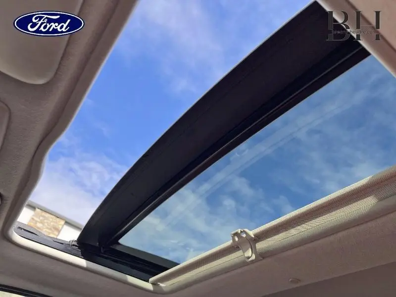 Toit ouvrant panoramique ouvert vu de l'intérieur d'une FIAT 500 noire, avec ciel bleu visible à travers.