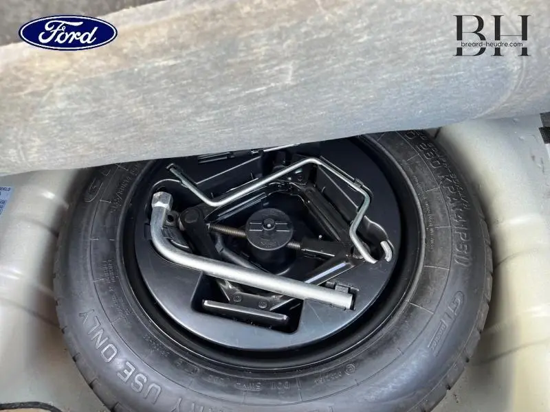 Vue rapprochée du pneu de secours avec outils de changement dans le coffre d'une Fiat 500 noire.