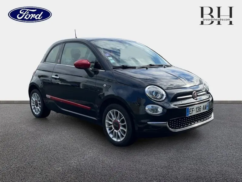 Vue 3/4 avant droite d'une Fiat 500 noire avec détails rouges sur les rétroviseurs et bas de porte, jantes alu visibles.