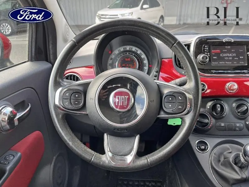 Vue intérieure centrée sur le volant cuir multifonction et tableau de bord rouge brillant d'une Fiat 500 noire de 2016.
