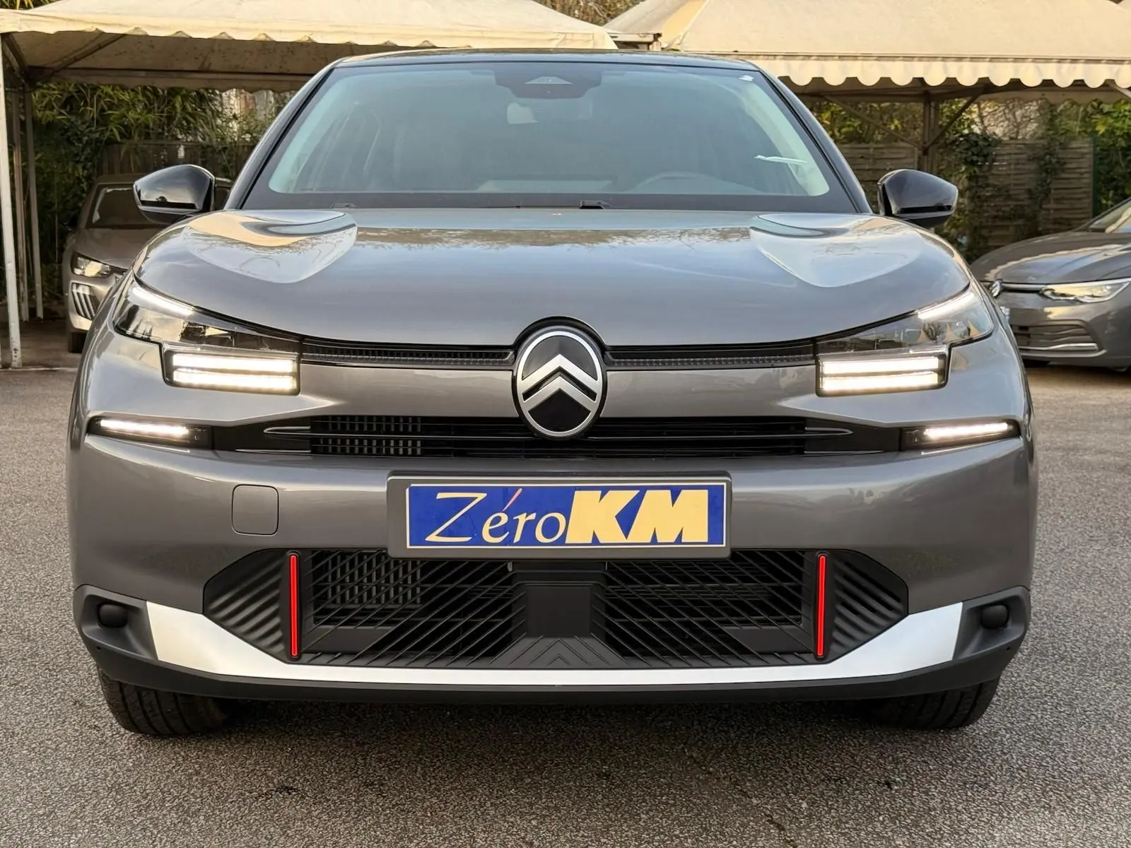Vue de face d'une Citroën C4 hybride gris Mercury avec phares LED allumés et détails rouges sur la calandre.