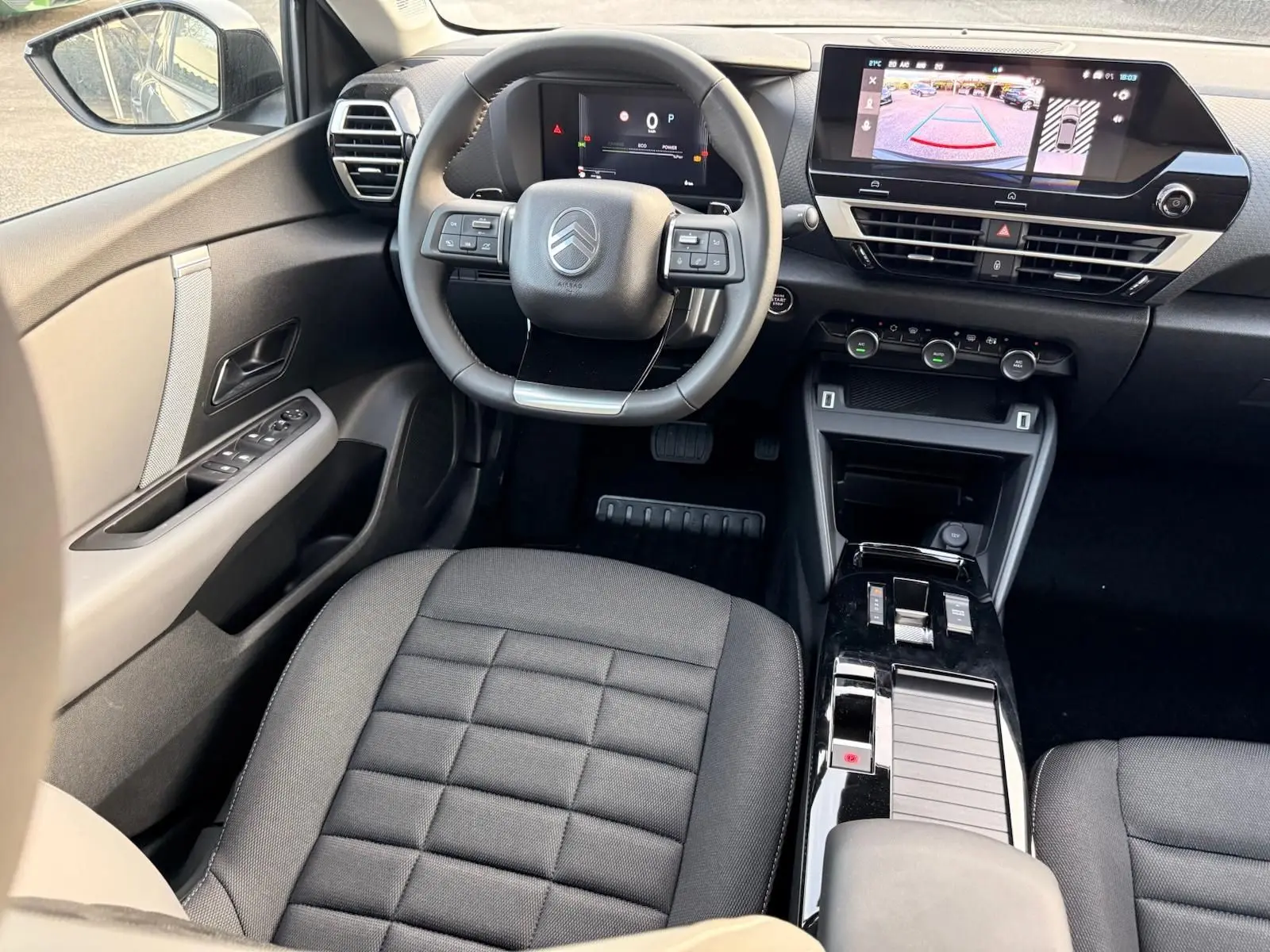 Vue intérieure avant centrée sur le volant et la console centrale noire du Citroën C4 hybride 2025 avec écran tactile affichant la caméra de recul.