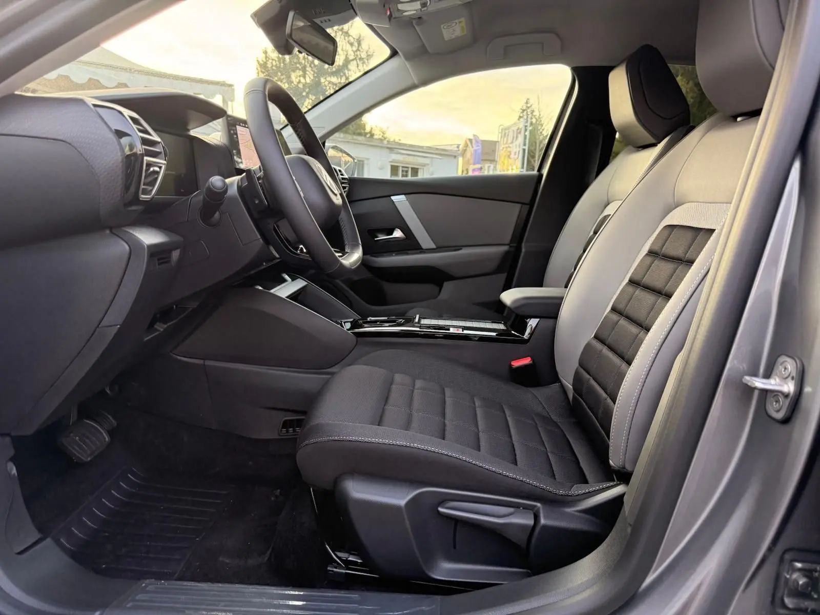 Vue intérieure côté conducteur du Citroën C4 hybride 2025 gris Mercury, mettant en valeur les sièges bi-ton et le tableau de bord moderne.