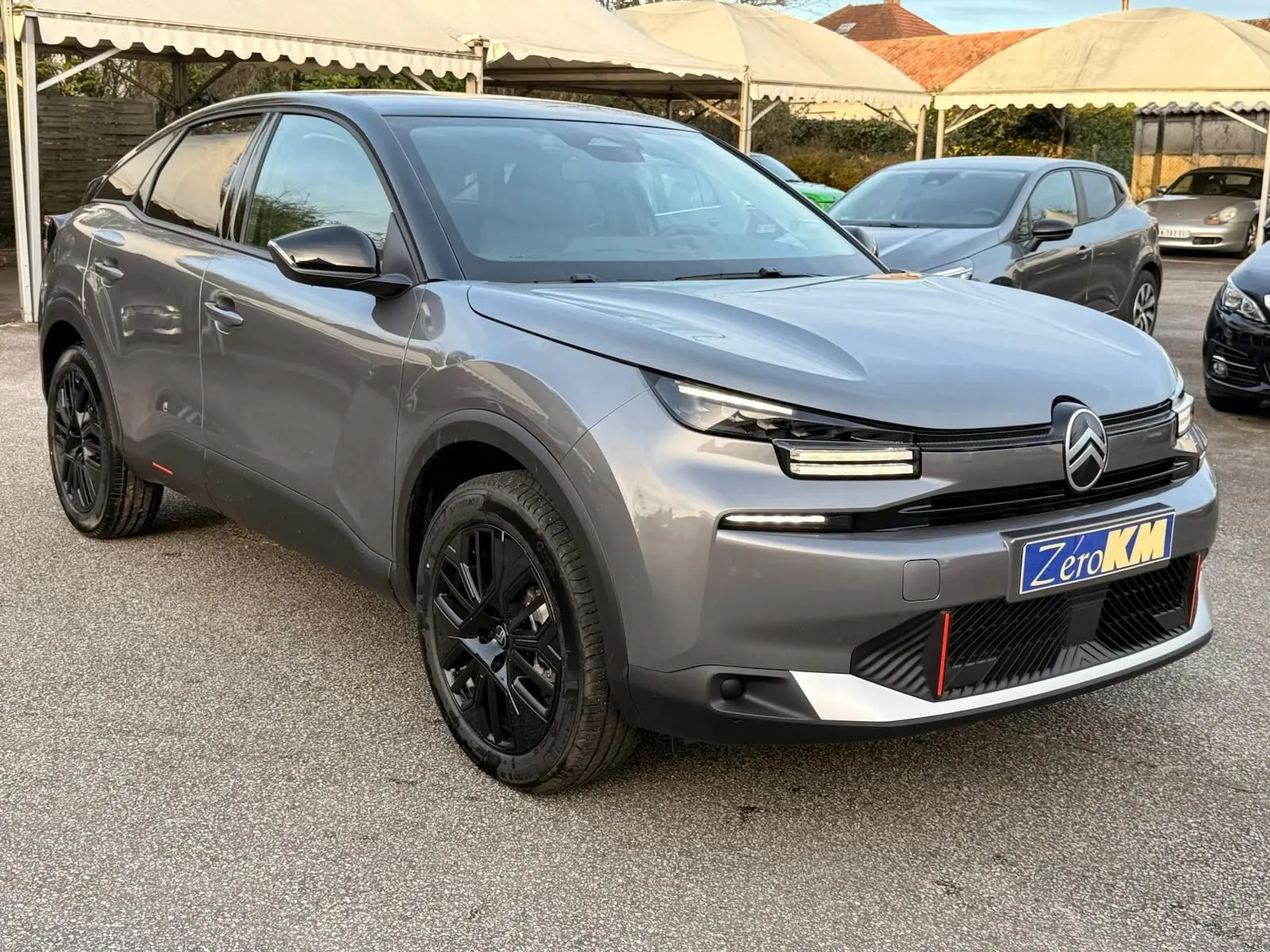 Citroën C4 hybride gris Mercury en 3/4 avant droit, avec jantes noires et signature lumineuse LED distinctive.