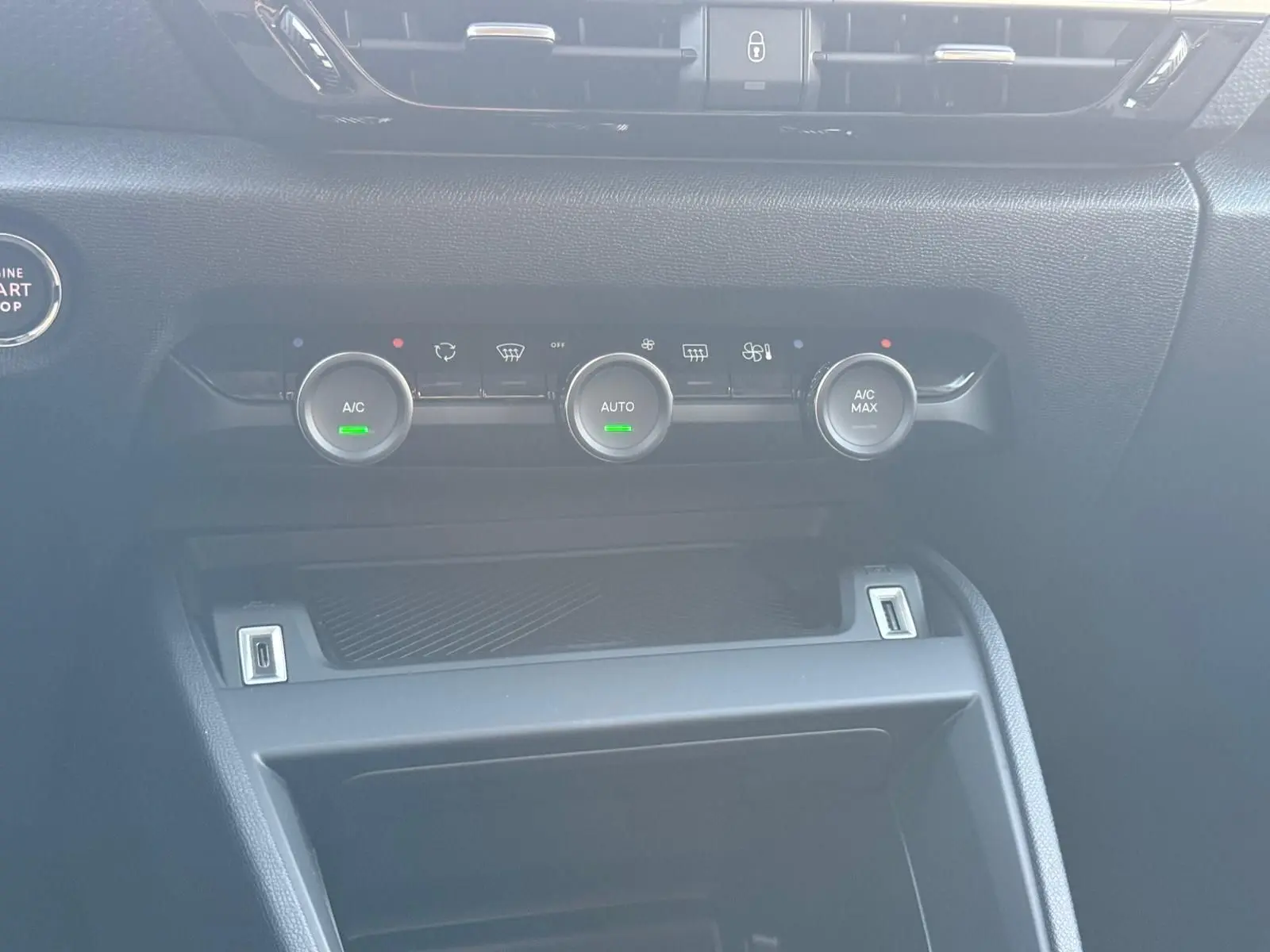 Gros plan sur la console centrale noire du Citroën C4 hybride 2025, avec commandes de climatisation et bouton start/stop.