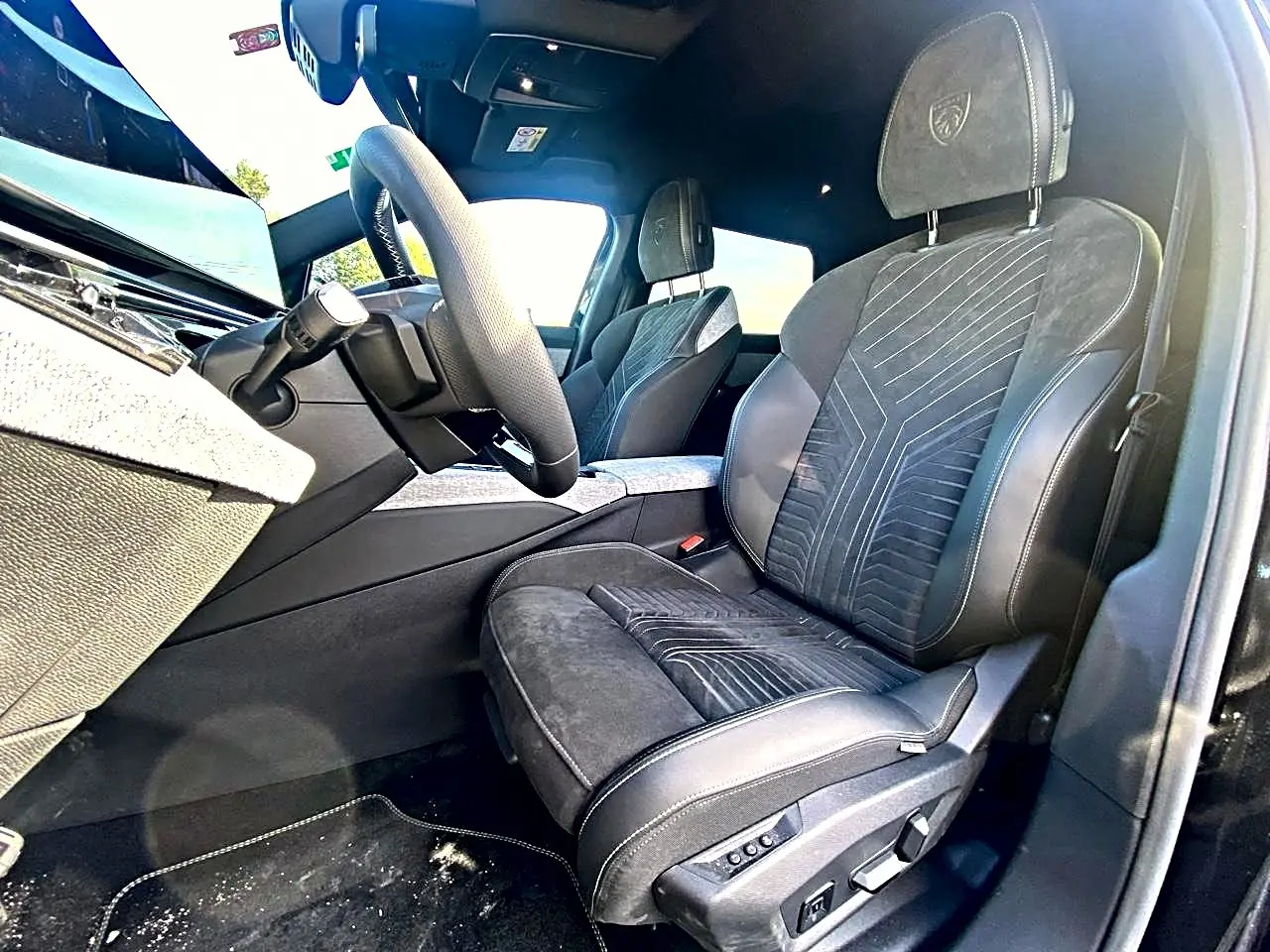 Vue intérieure côté conducteur du Peugeot 5008 Hybrid 145 GT e-dcs6 2025, sièges noirs avec surpiqûres et logo Peugeot brodé.