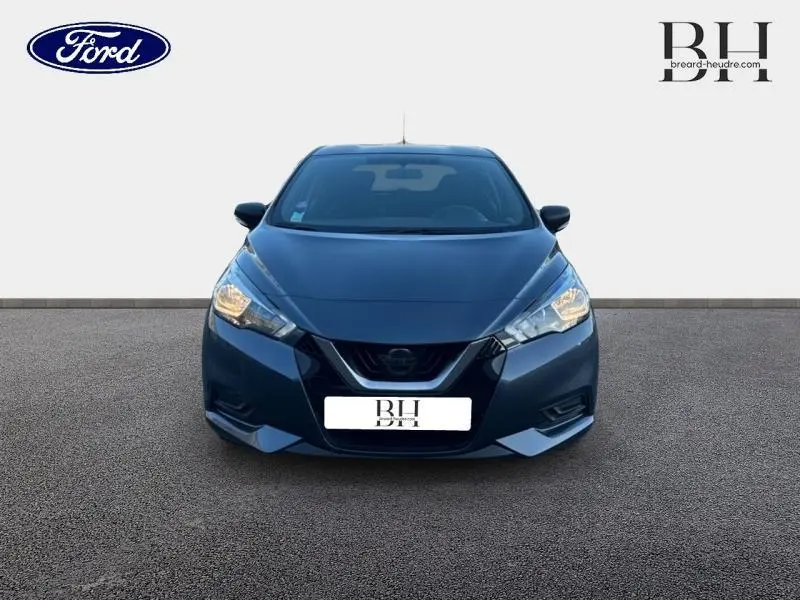 Vue frontale d'une Nissan Micra 1.0 71ch Visia Pack gris acier avec phares allumés sur fond neutre.