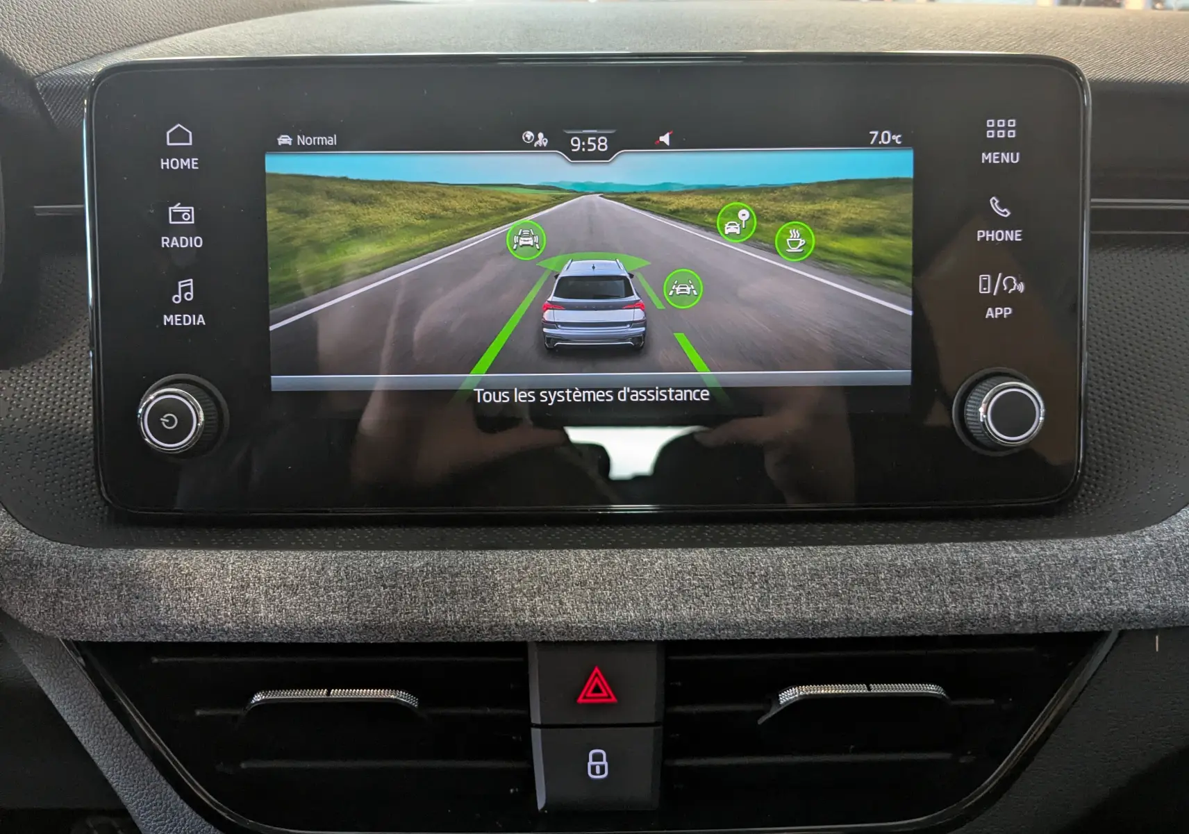 Écran central tactile du Skoda Kamiq 2025 montrant l'affichage des systèmes d'assistance sur fond de route virtuelle.