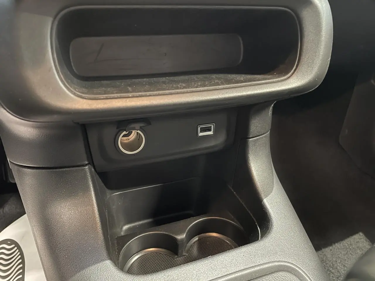 Gros plan sur la console centrale noire avec prise USB et allume-cigare dans une Citroën C3 gris foncé.