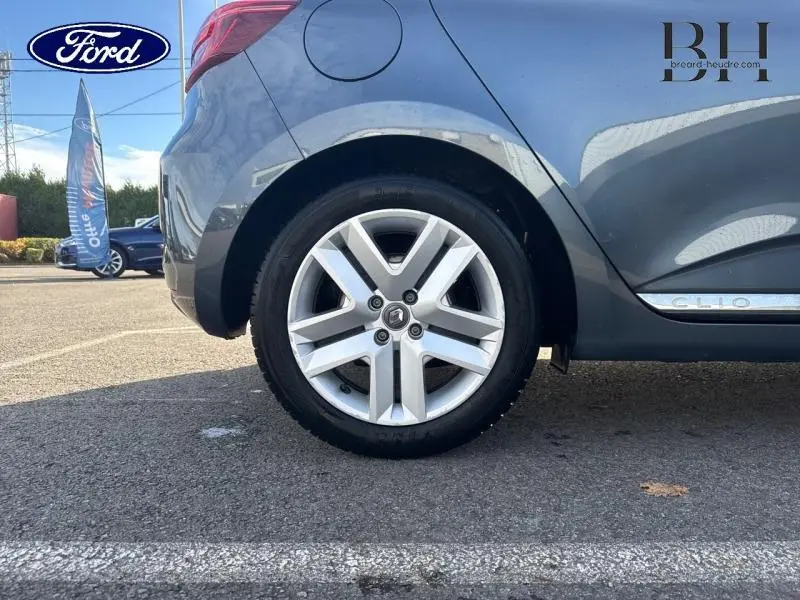 Gros plan sur la roue arrière droite d'une Renault Clio gris Titanium avec jante alliage et logo Renault visible sur le cache central.