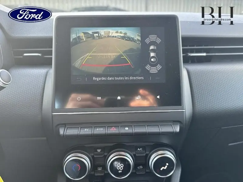 Vue intérieure du tableau de bord de la Renault Clio hybride 2021 avec écran tactile affichant la caméra de recul et commandes climatisation.