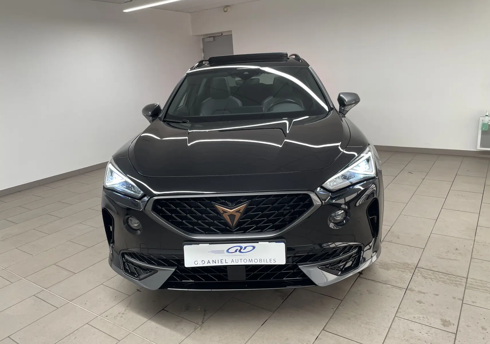 Vue frontale d'un CUPRA Formentor 1.5 TSI 150 DSG7 VZ-LINE noir minuit avec calandre distinctive et phares allumés.