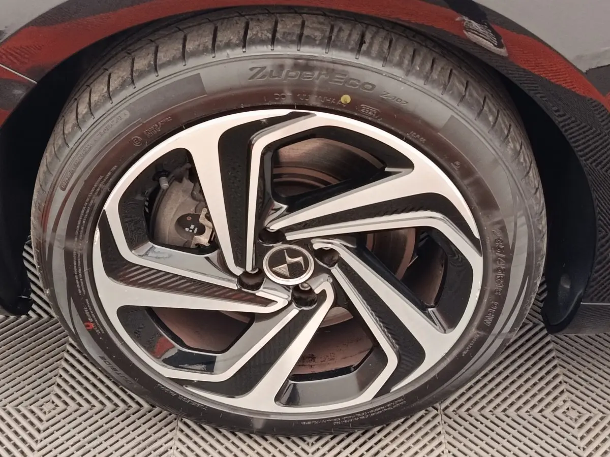 Gros plan sur la roue avant droite d'une DS5 noire, mettant en valeur la jante en alliage au design moderne bicolore.