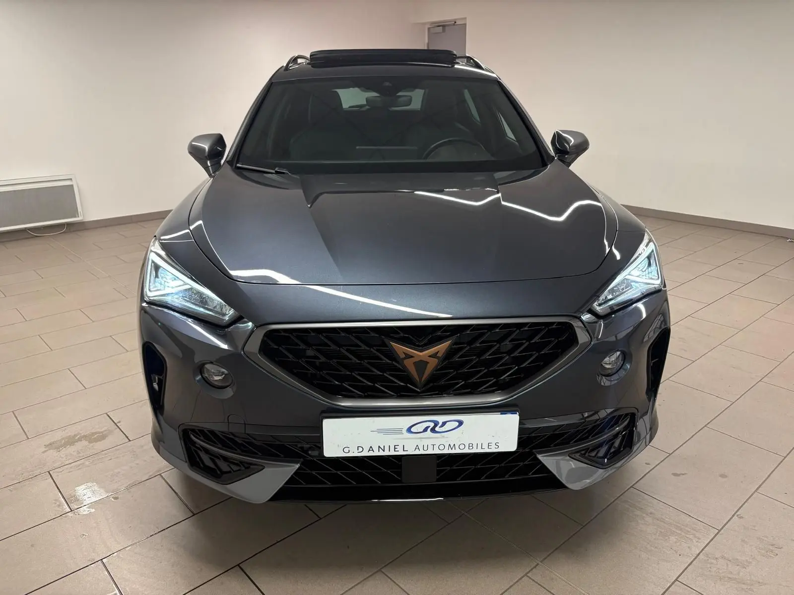 Vue frontale d'un CUPRA Formentor 1.5 TSI 150 DSG7 VZ-LINE gris magnétique avec calandre noire et logo cuivré.