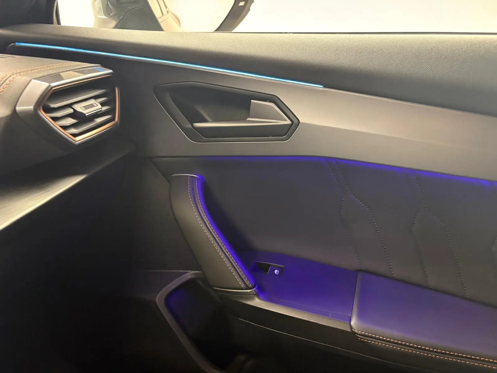 Intérieur côté passager du CUPRA Formentor 2023, montrant la porte avec éclairage d'ambiance bleu et surpiqûres marron.
