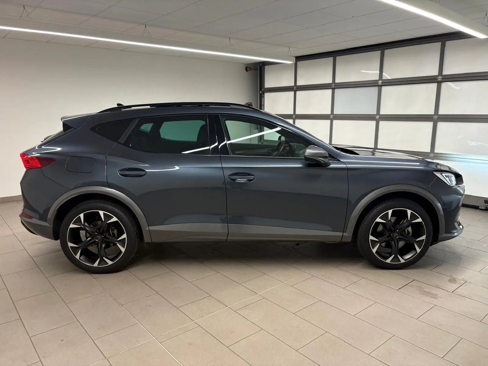 Vue de profil côté gauche d'un CUPRA Formentor 2023 gris magnétique avec jantes noires et détails sportifs en intérieur.