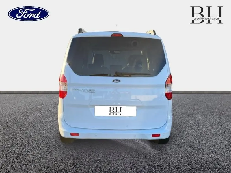 Vue arrière d'un Ford Tourneo Courier blanc Glacier avec hayon et vitres arrière teintées sur sol gris.