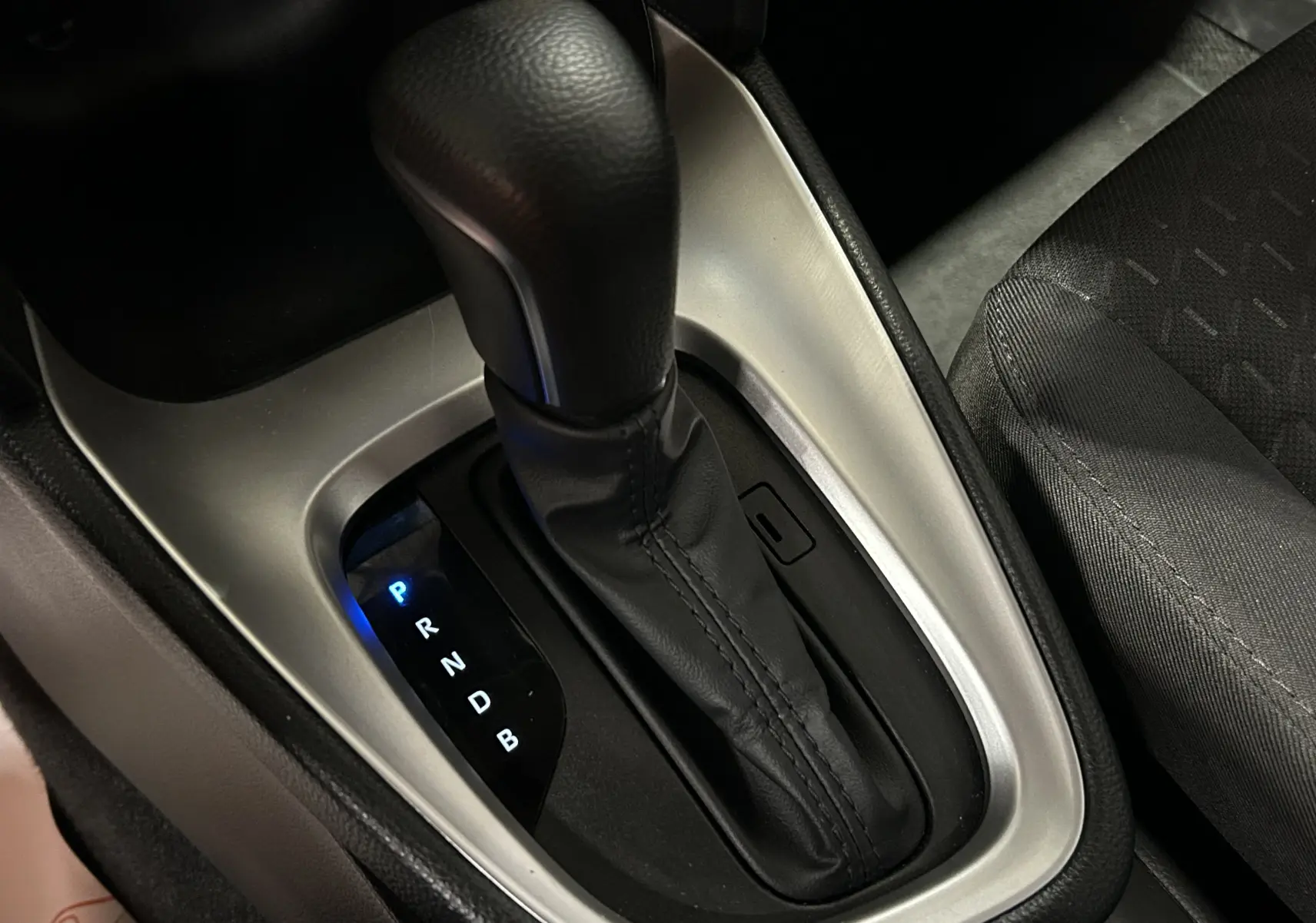 Gros plan sur le levier de vitesses automatique noir et argenté de la Toyota Yaris Cross, avec siège tissu gris visible à droite.