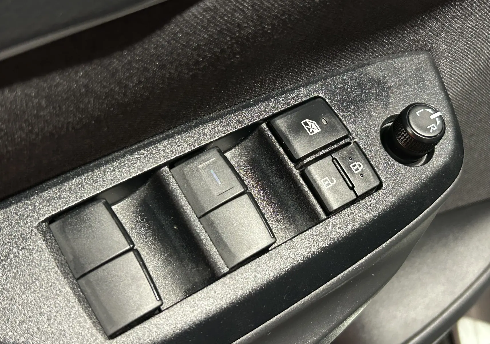 Gros plan sur les commandes des vitres et rétroviseurs côté conducteur de la Toyota Yaris Cross 2025 gris minéral.