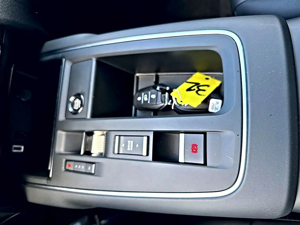Vue rapprochée de la console centrale grise avec bouton de frein à main électrique et clé de voiture Citroën C5 Aircross blanche.