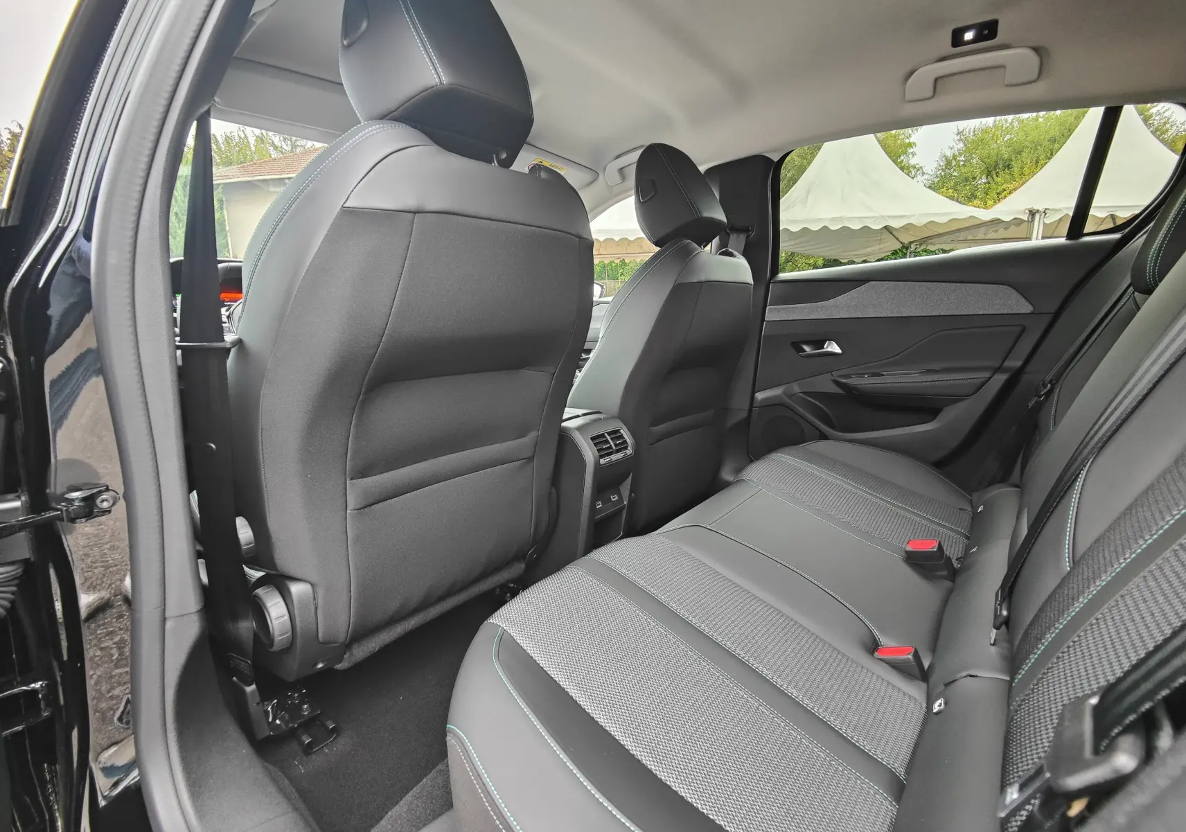 Vue intérieure arrière côté droit de la Peugeot 308 PureTech 130 Allure Pack 2023 noire, sièges en tissu et cuir avec surpiqûres bleues.