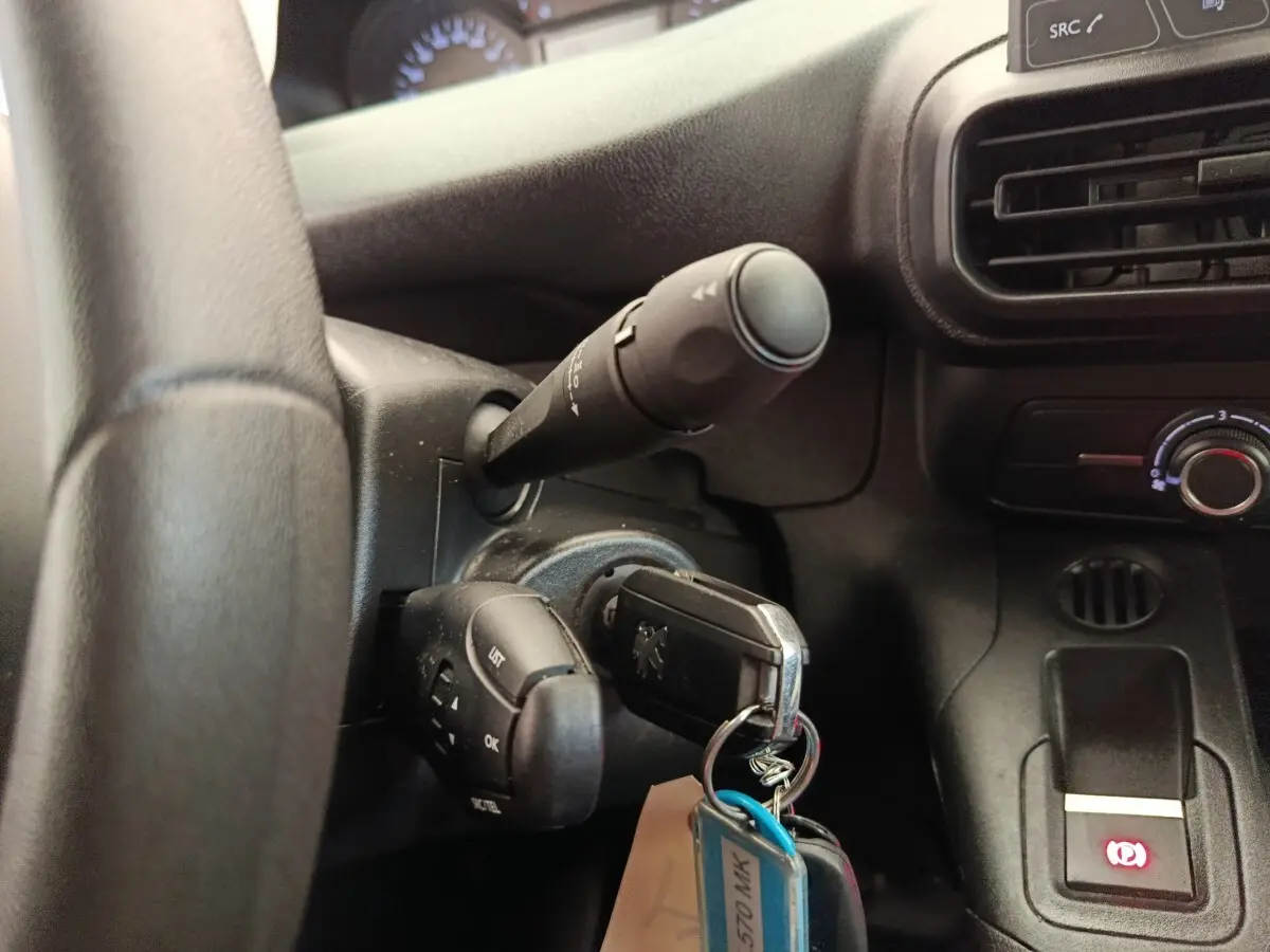 Gros plan sur le volant noir et la clé insérée dans le contact d’un Peugeot Partner blanc, avec commandes au volant visibles.