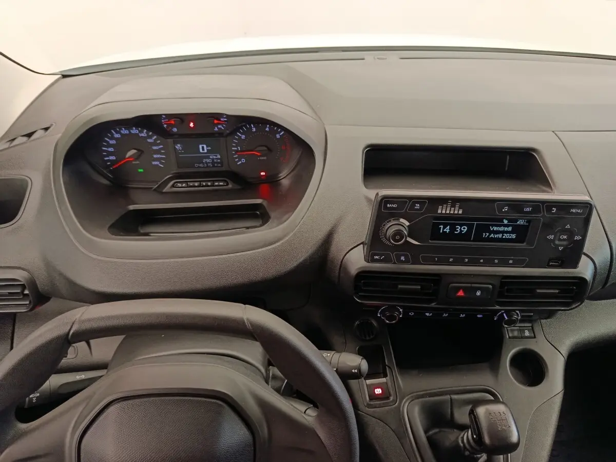 Vue intérieure du tableau de bord et volant noir du Peugeot Partner blanc, avec écran radio et commandes manuelles visibles.