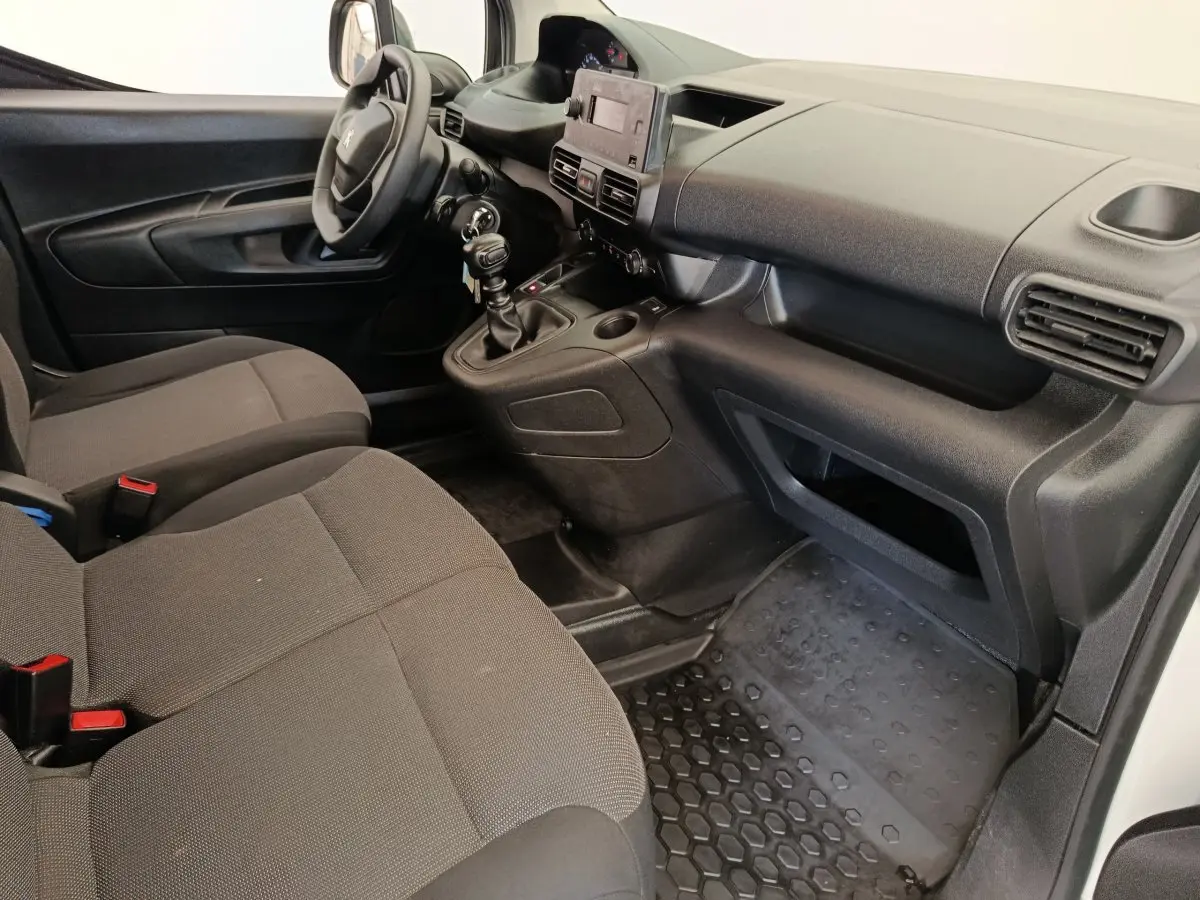 Vue intérieure côté conducteur du Peugeot Partner 2022, montrant les sièges gris, le volant et la console centrale avec boîte manuelle.