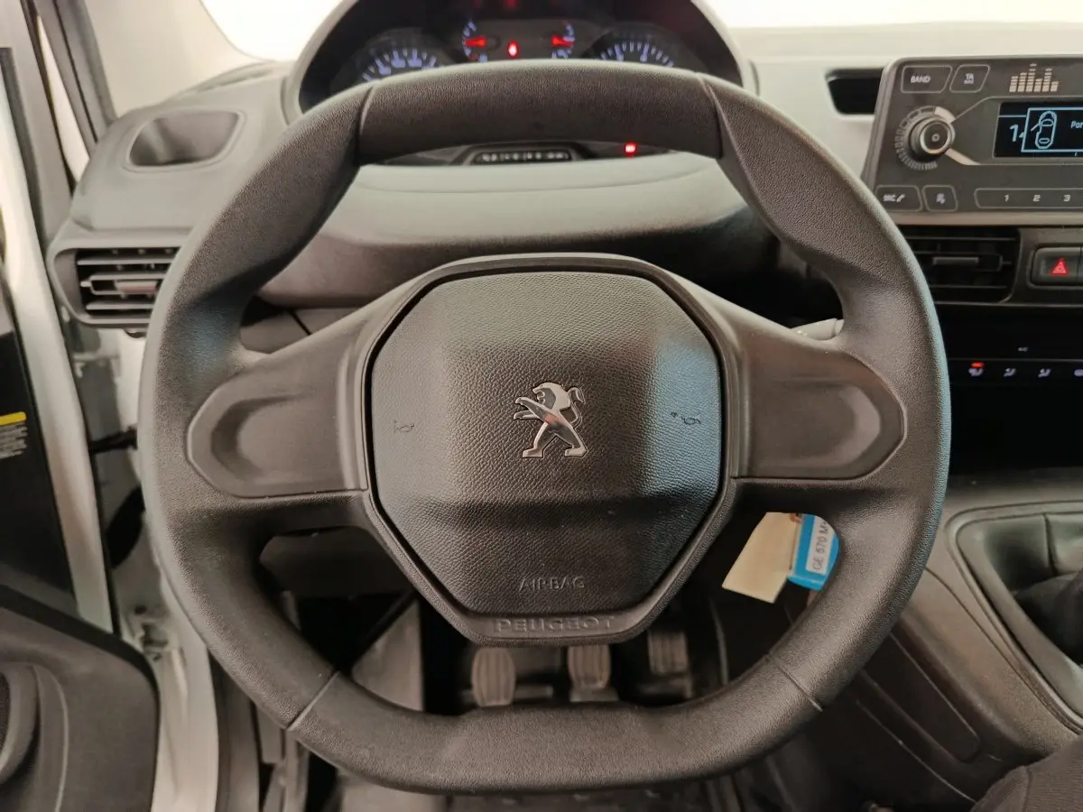 Vue rapprochée du volant noir de la Peugeot Partner 2022, avec tableau de bord et console centrale visibles en arrière-plan.