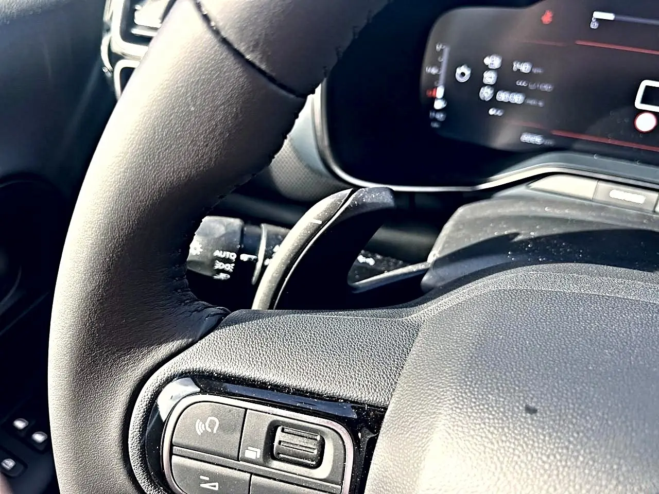 Gros plan sur le volant cuir noir du Citroën C5 Aircross 2025 avec commandes multifonctions et tableau de bord numérique flou.