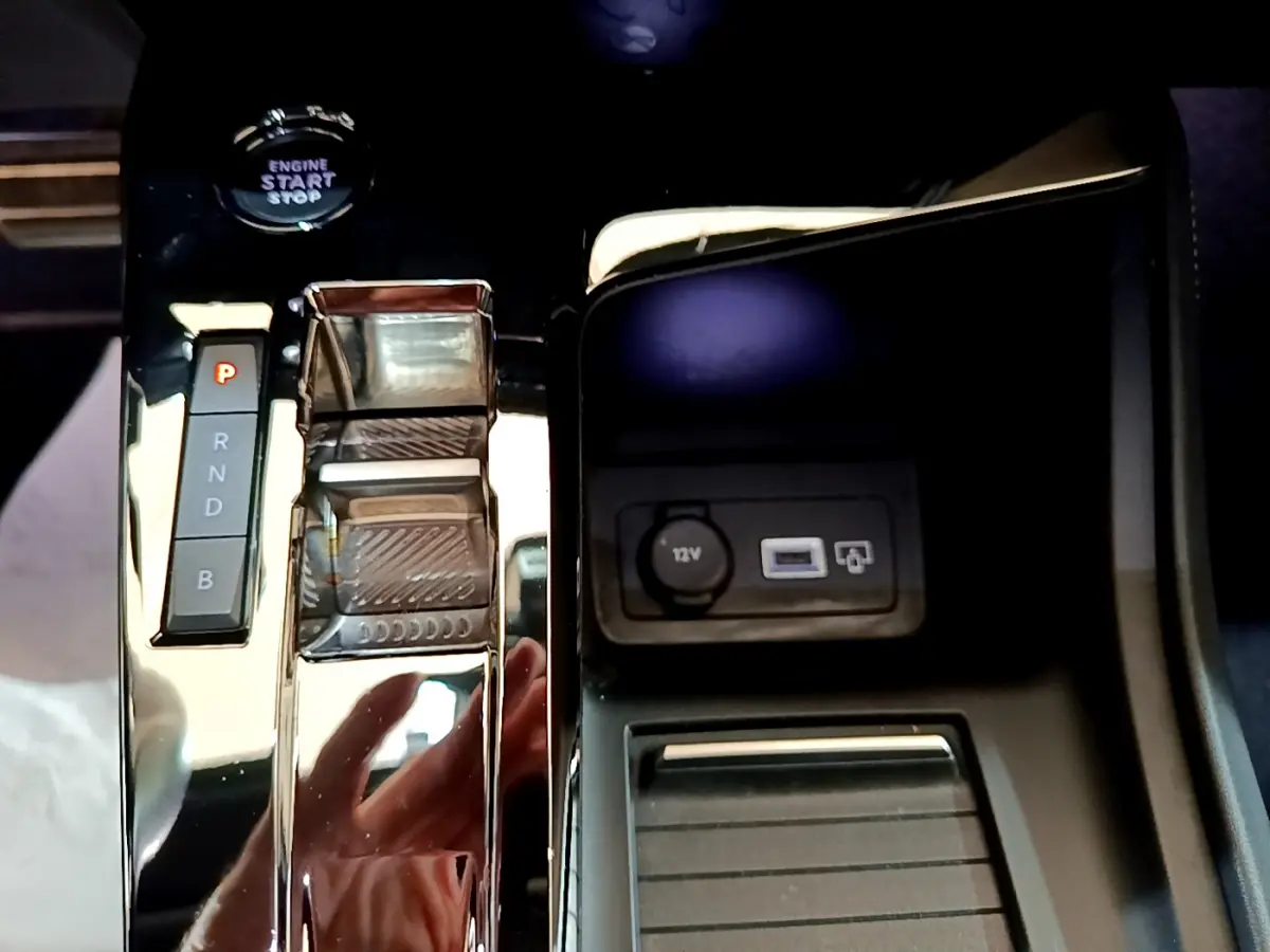 Gros plan sur la console centrale noire brillante de la Peugeot 308 PHEV 180 E-EAT8 GT avec sélecteur de boîte auto et prise 12V.