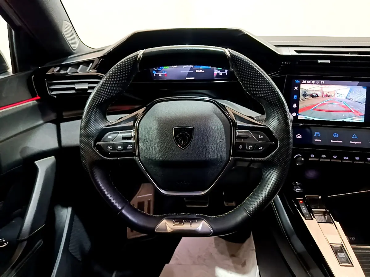 Vue intérieure centrée sur le volant cuir noir GT et tableau de bord numérique de la Peugeot 308 PHEV blanche 2022.