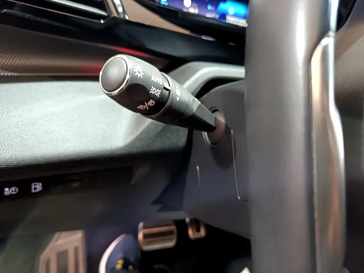 Gros plan sur la manette des phares côté gauche du volant cuir noir dans l'habitacle de la Peugeot 308 PHEV blanche 2022.