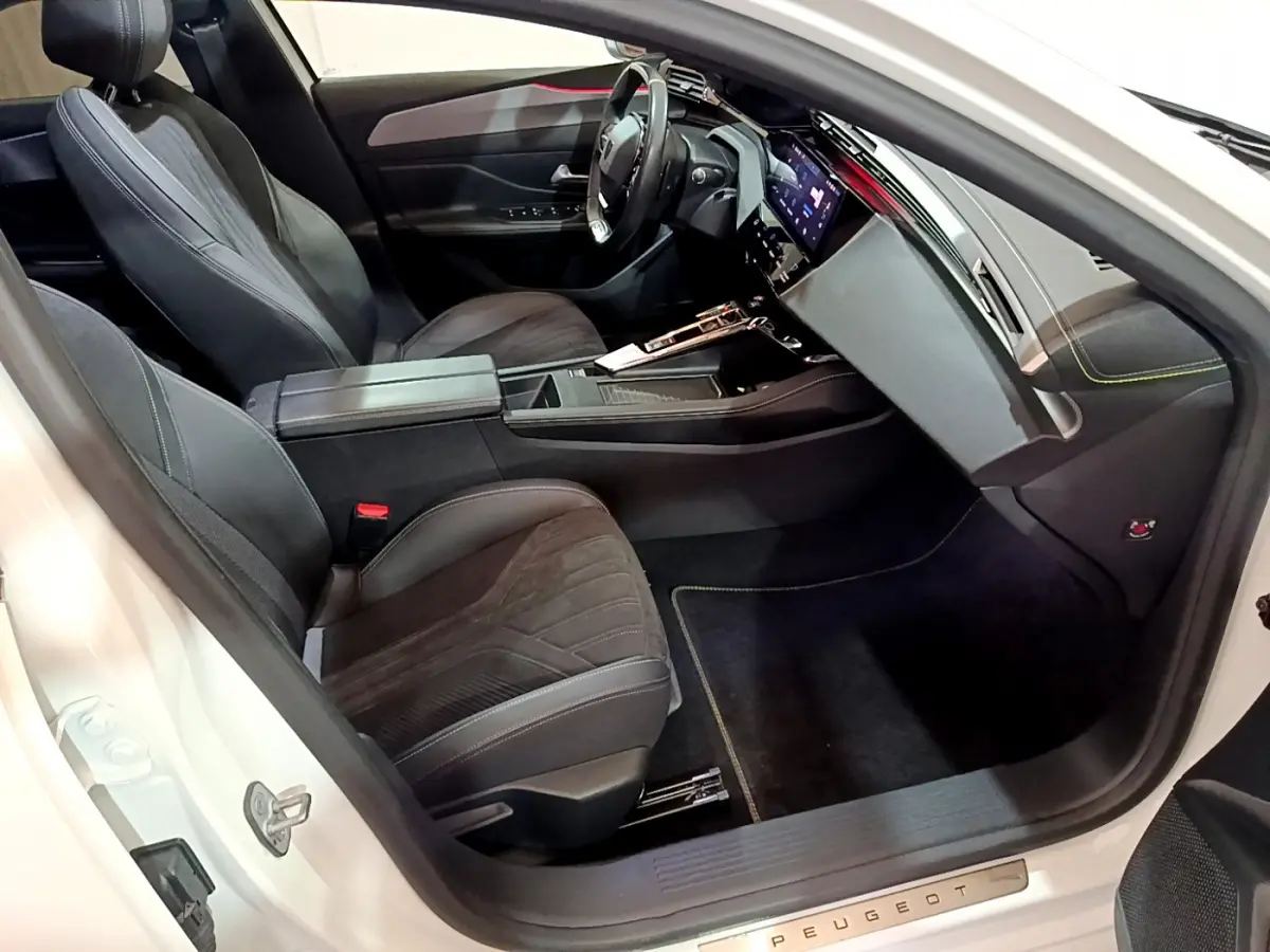 Intérieur avant droit de la Peugeot 308 PHEV 180 GT blanche, avec sièges noirs et tableau de bord digital.