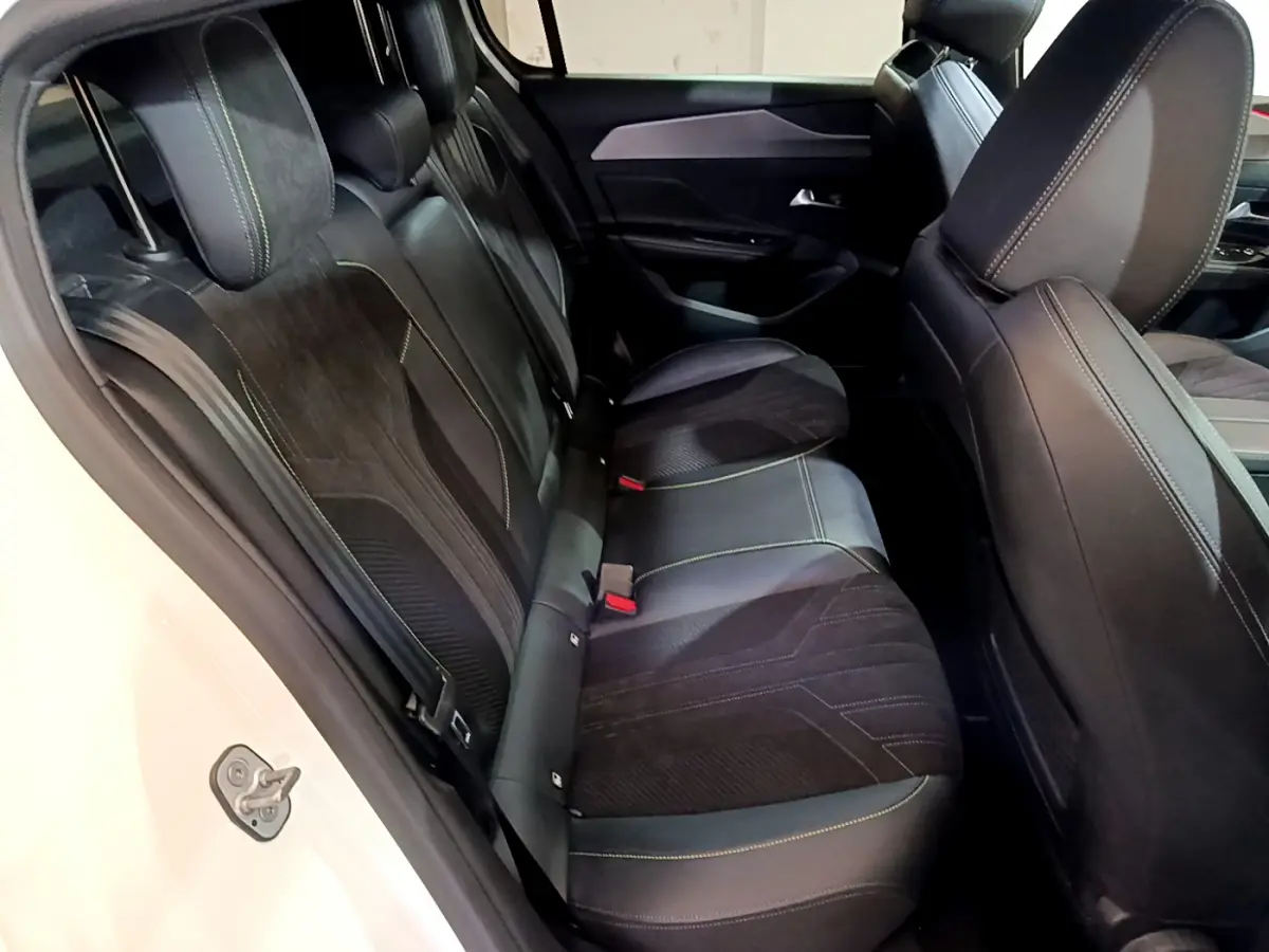 Vue côté gauche sur les sièges arrière noirs avec surpiqûres vertes d'une Peugeot 308 PHEV 180 E-EAT8 GT blanche.