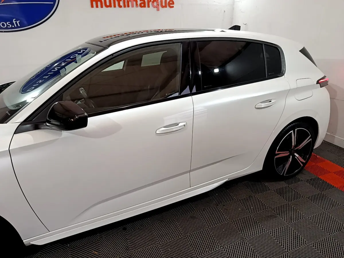 Profil droit d'une Peugeot 308 PHEV 180 E-EAT8 GT blanche avec vitres teintées et jantes noires stylisées.