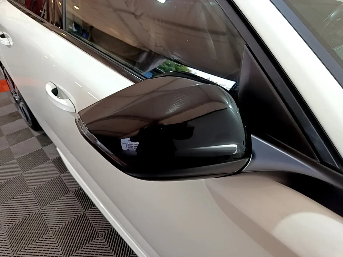 Rétroviseur noir brillant côté gauche d'une Peugeot 308 PHEV 180 E-EAT8 GT blanche vue en gros plan.