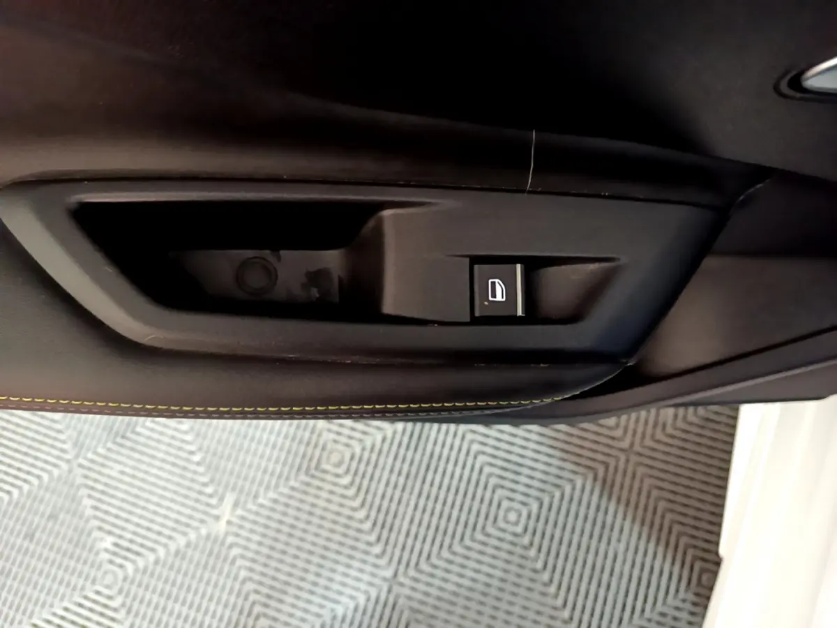 Bouton de commande de verrouillage des portes sur la garniture intérieure noire avec surpiqûres jaunes d'une Peugeot 308 PHEV 180 E-EAT8 GT blanche.