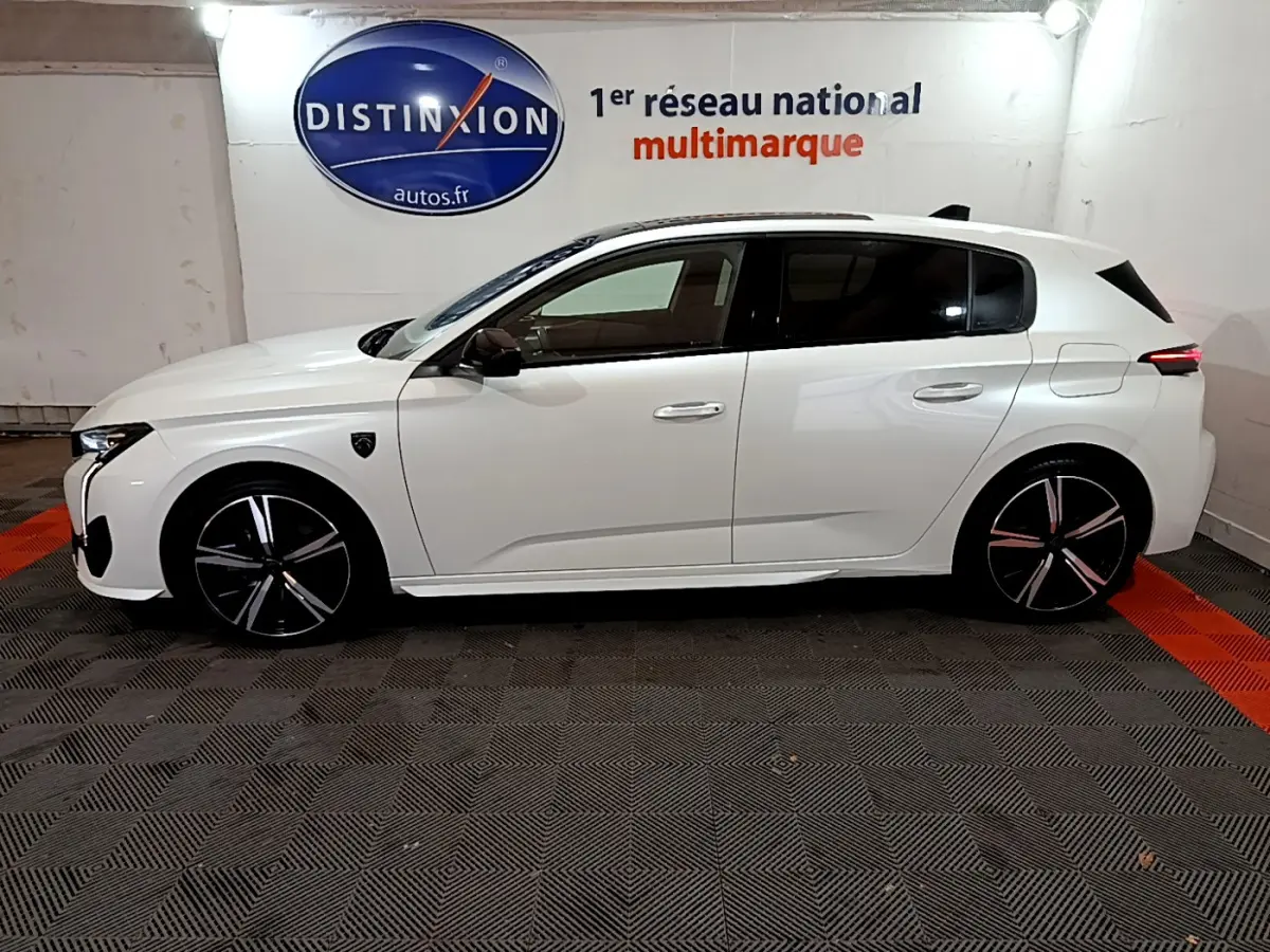 Profil côté gauche d'une Peugeot 308 PHEV 180 E-EAT8 GT blanche, avec jantes noires et logo Distinxion en arrière-plan.