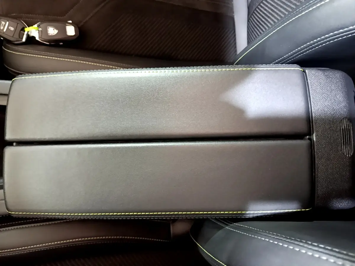 Gros plan sur l'accoudoir central noir avec surpiqûres vertes dans l'habitacle d'une Peugeot 308 PHEV 180 E-EAT8 GT.