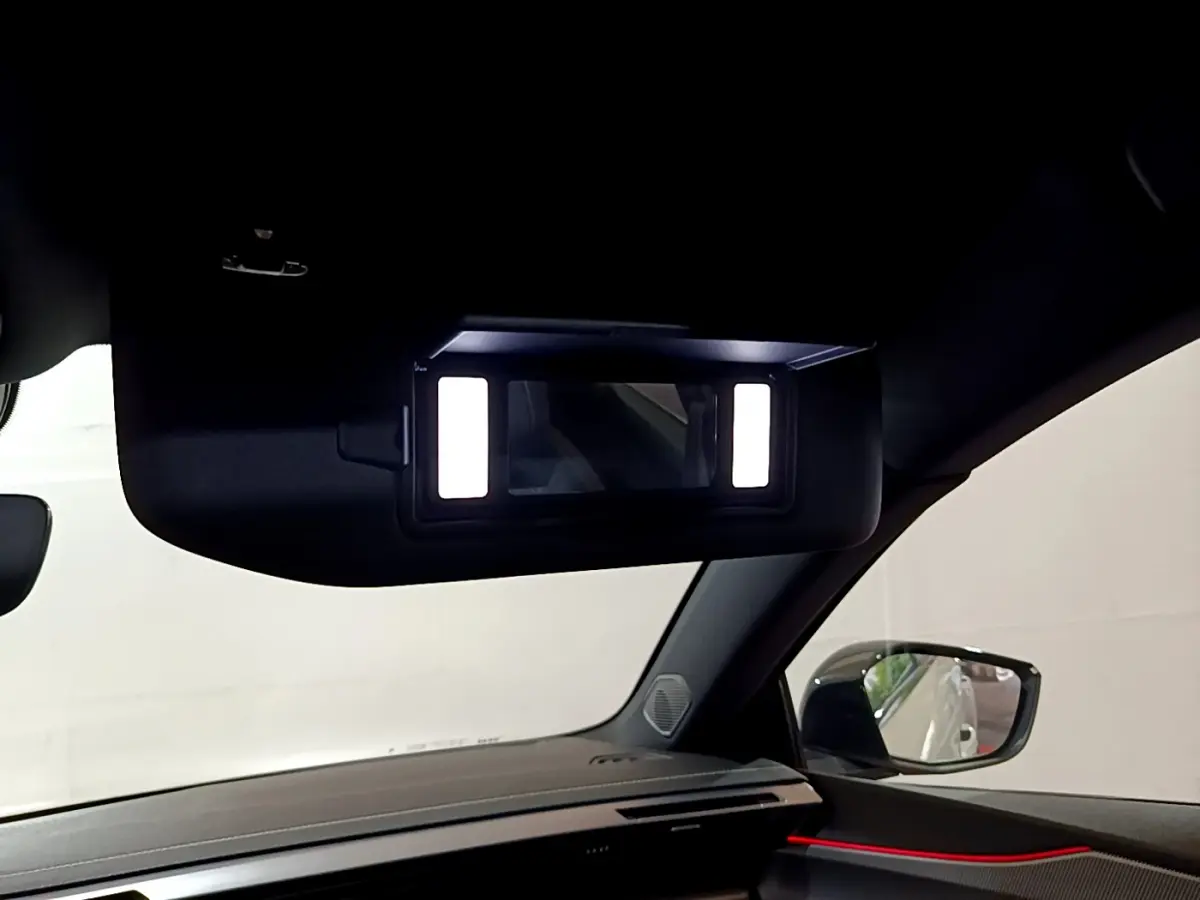 Détail du miroir de courtoisie éclairé côté passager dans l'habitacle sombre d'une Peugeot 308 PHEV blanche.