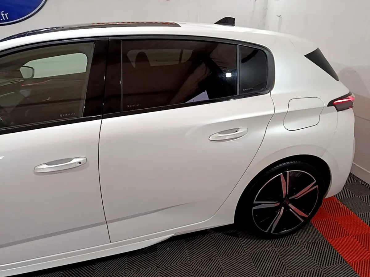 Vue latérale droite de la Peugeot 308 PHEV 180 E-EAT8 GT blanche, soulignant la porte arrière et la jante noire à motifs rouges.