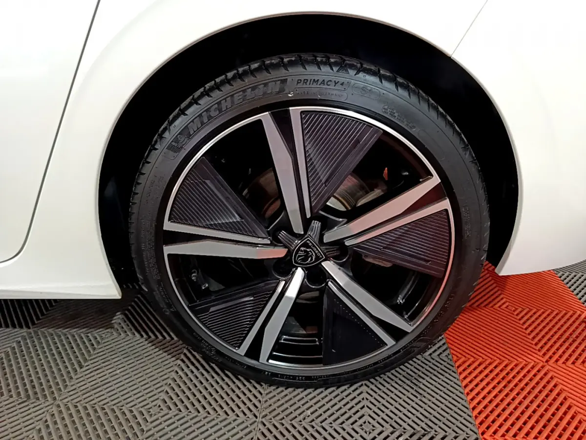 Gros plan sur la roue arrière droite blanche d'une Peugeot 308 PHEV 180 E-EAT8 GT avec jante noire et argentée design moderne.